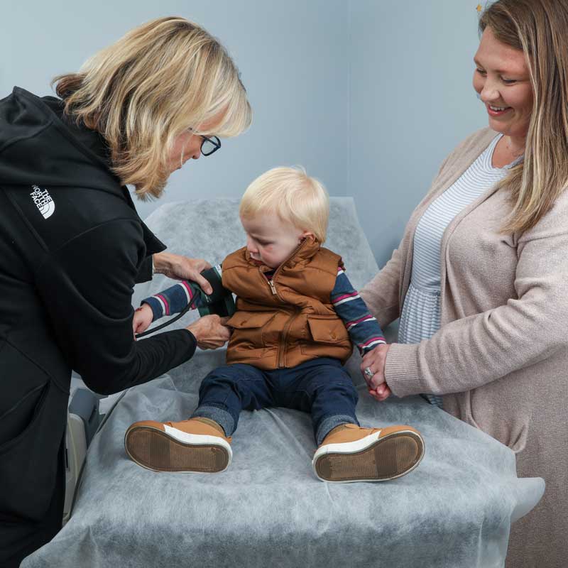 a health care provider measures a toddler's blood pressure with a stethoscope with the help of the child's mother