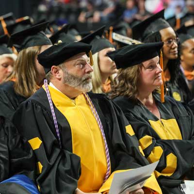 v.c.u. school of nursing faculty dressed in regalia listening to a graduation ceremony speech