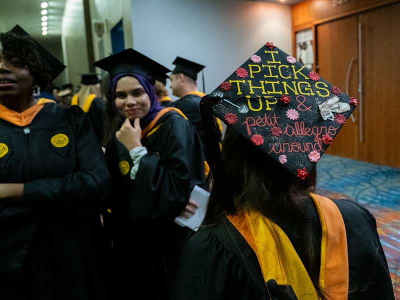 v.c.u. school of nursing graduates dressed in commencement regalia  with one student wearing a graduation cap decorated with the words i pick things up and petit allegro around