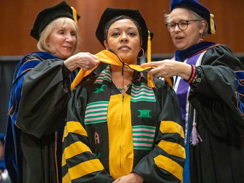 samantha thomas dressed in regalia at the v.c.u. school of nursing ceremony being hooded by two faculty members